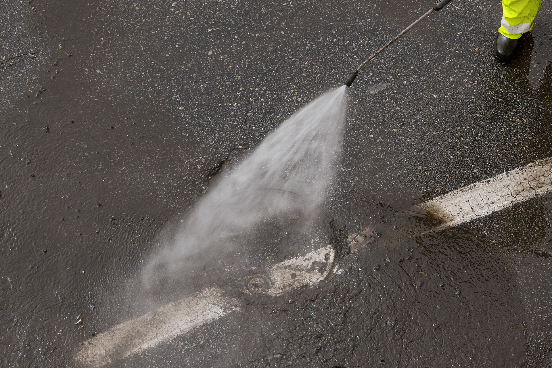 Worker cleaning a city road with high pressure water jet machine